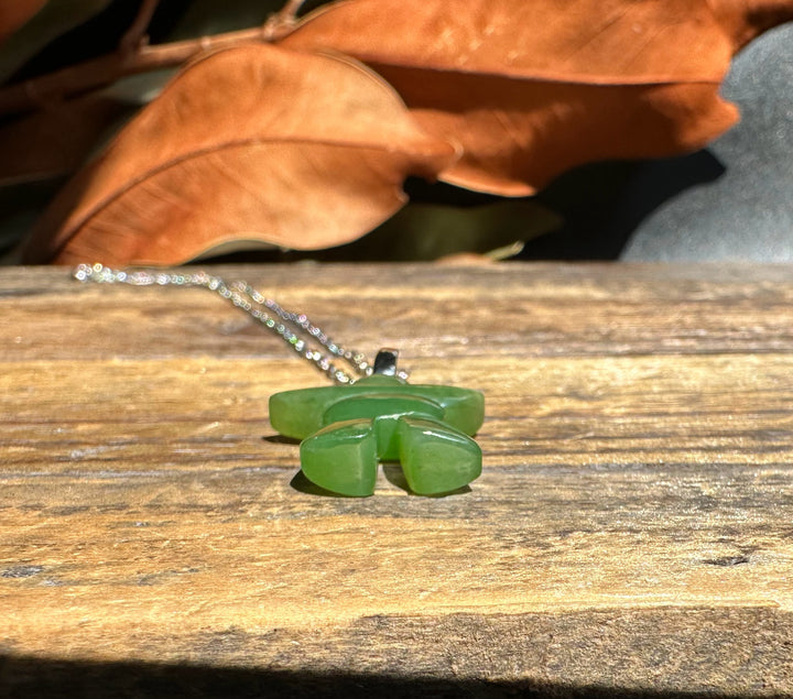 Green jade Inukshuk pendant with chain resting on a wooden surface