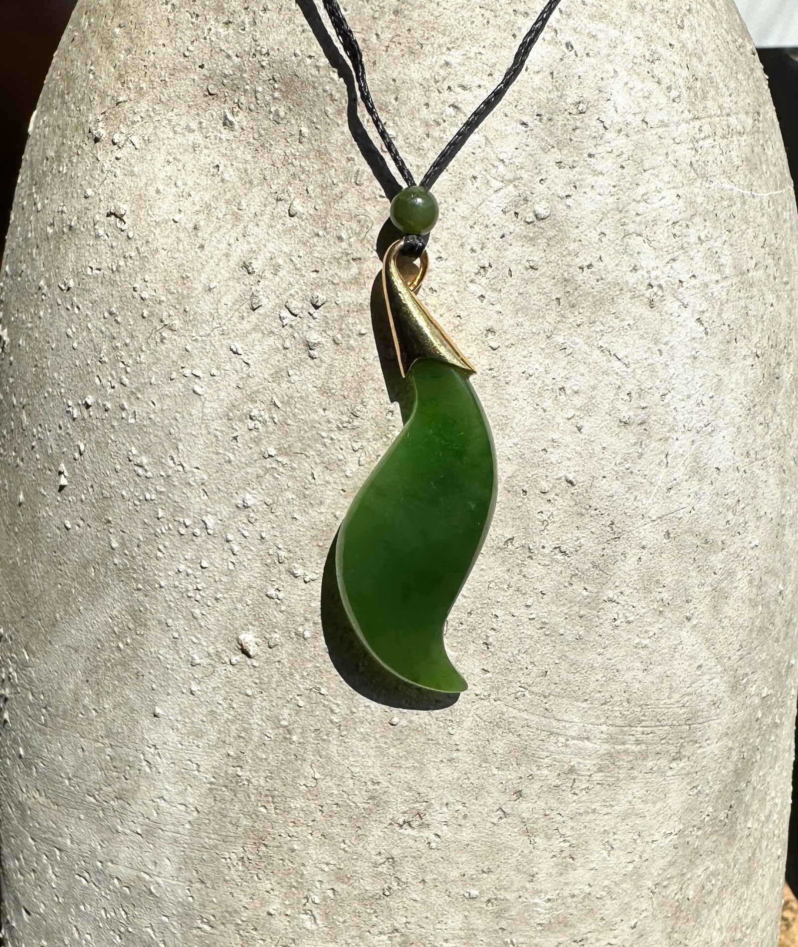Canadian nephrite jade pendant in a curved crescent shape with a brass bail on a black cord and a small green bead above
