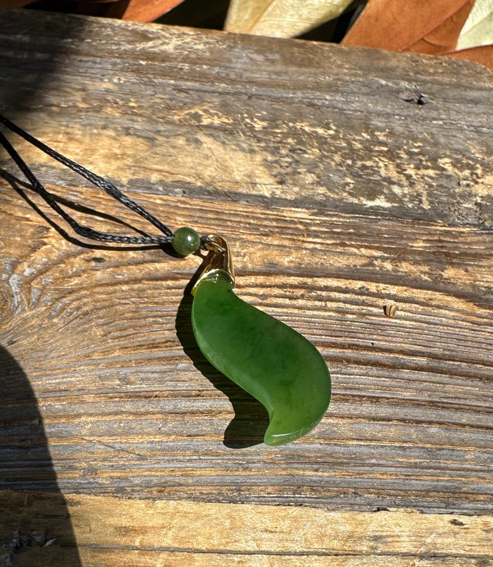 Bright green nephrite jade pendant on a black cord with a bead against weathered wood