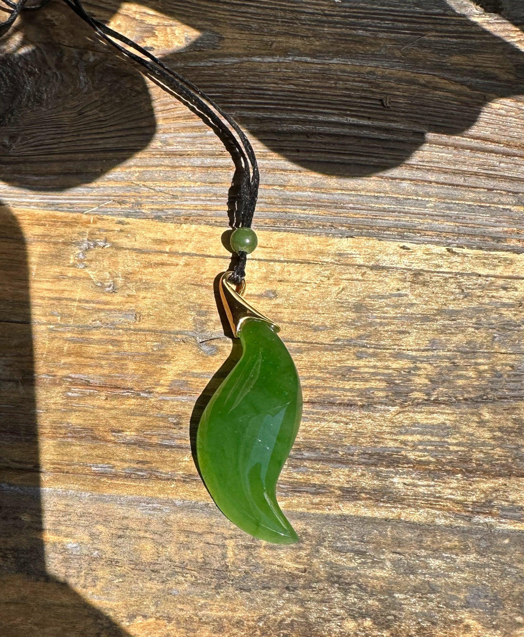 Green curved nephrite jade pendant with a gold bail on a black cord