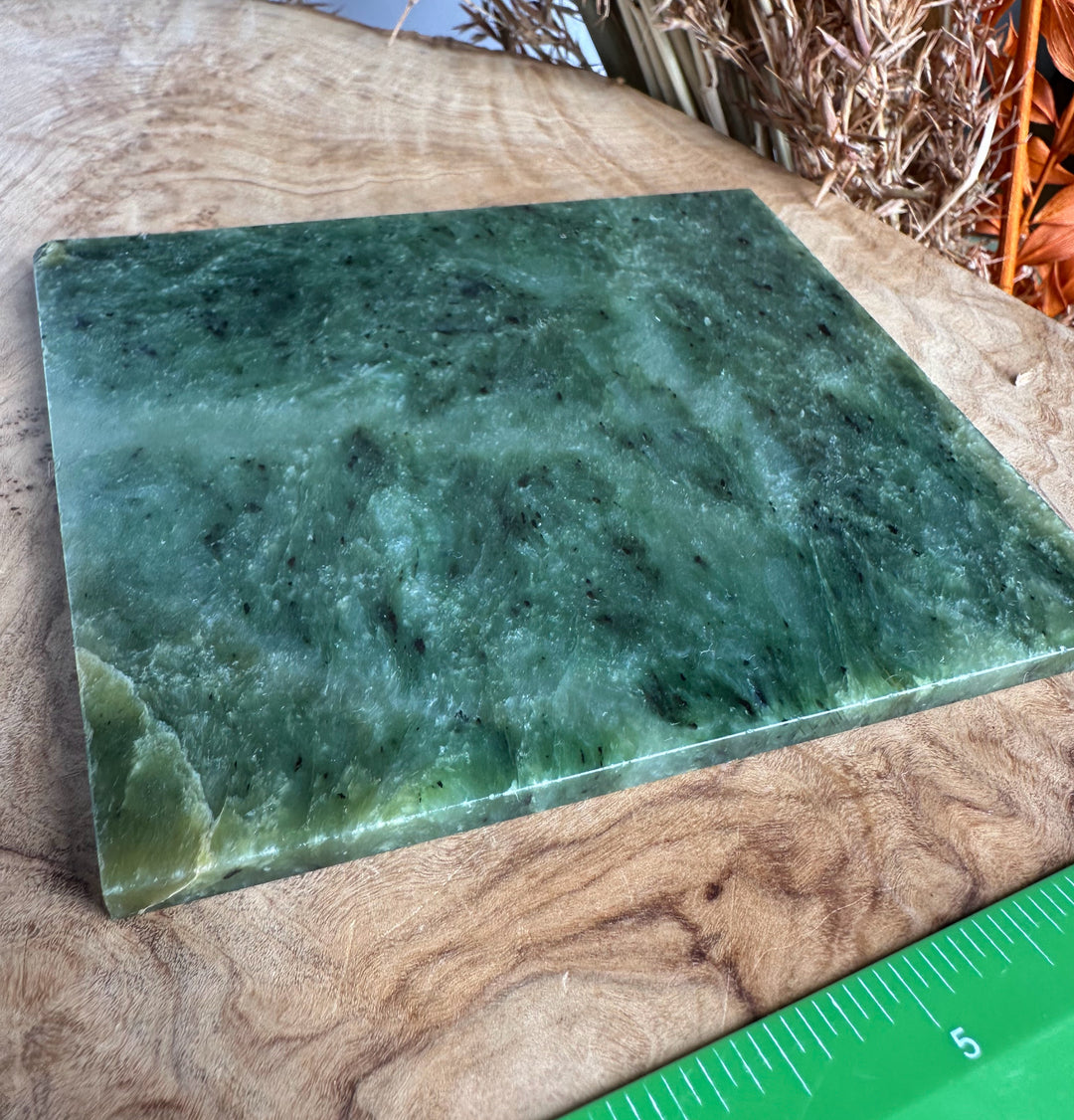 A green jade slab with natural marbled patterns, displayed on a wooden surface with a green measuring ruler visible in the corner for scale.