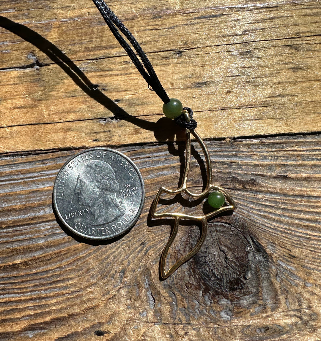 Vintage Jade and Brass Bird Pendant with a green bead near the head shown beside a quarter on a rustic wooden surface