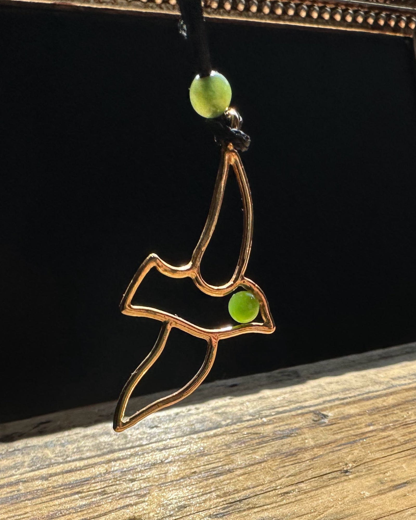 Gold brass bird pendant on black cord with two green jade beads.
