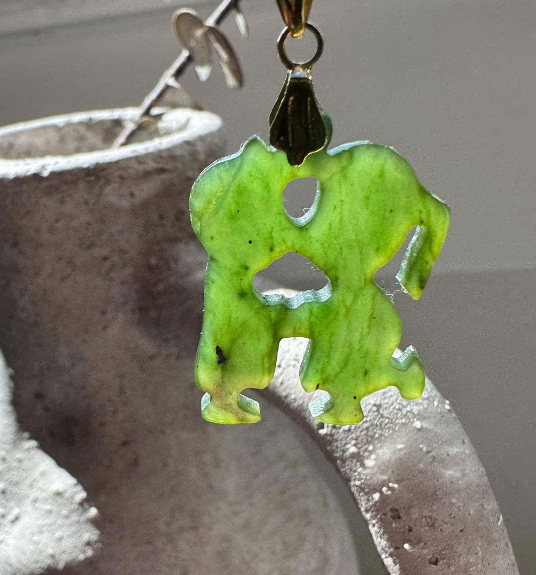 Close-up of lime green jade elephant pendant with cutout shapes and brass bail.
