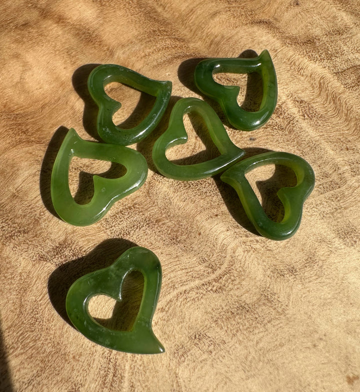Group of five translucent green jade heart pendants with hollow centers on brown fabric