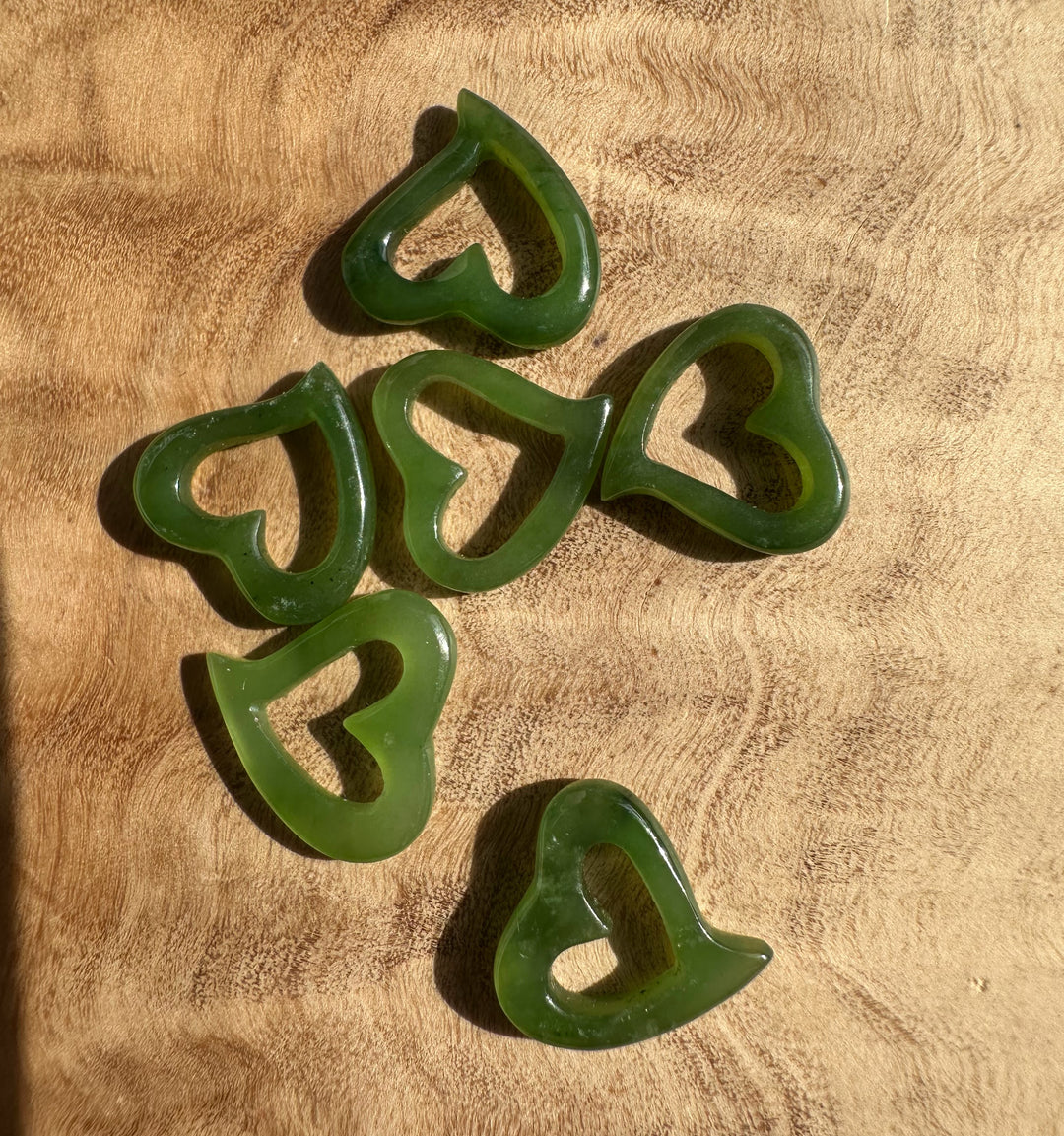 Five green jade heart pendants with hollow centers arranged on a wooden surface