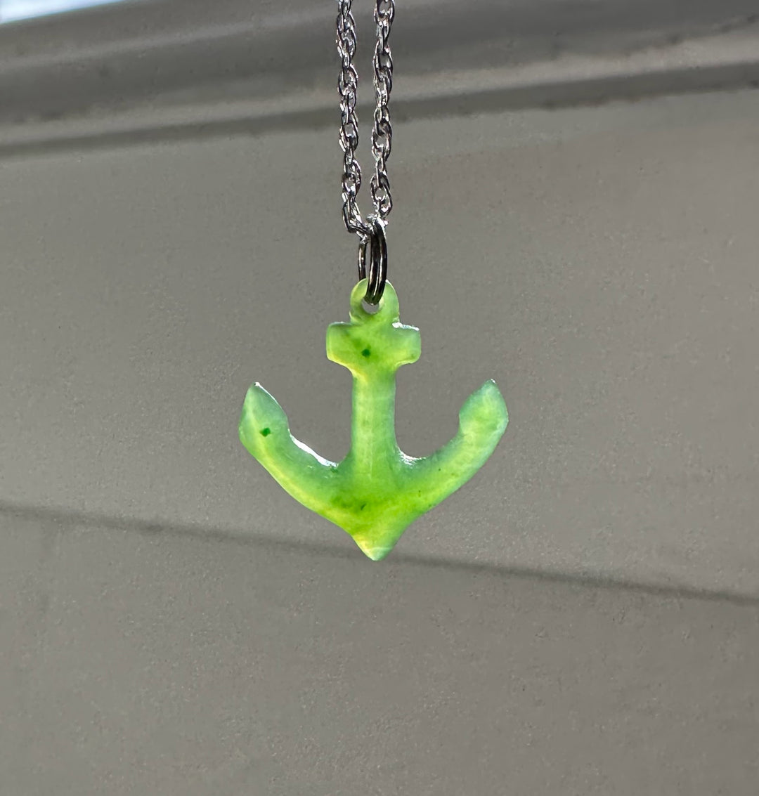 Bright green jade anchor pendant on a silver chain against a neutral background.