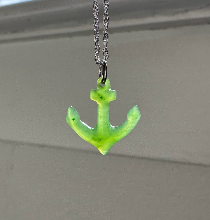Bright green jade anchor pendant on a silver chain against a neutral background.