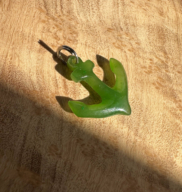 Green jade anchor charm with a silver jump ring on a wood background.