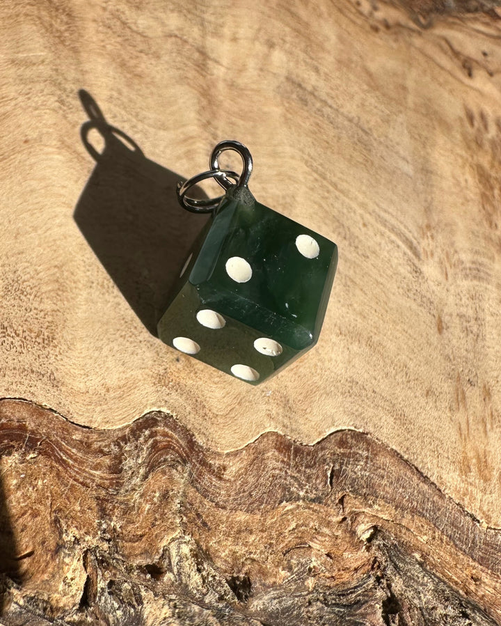 Green dice charm with white pips and a silver ring on a wooden surface.