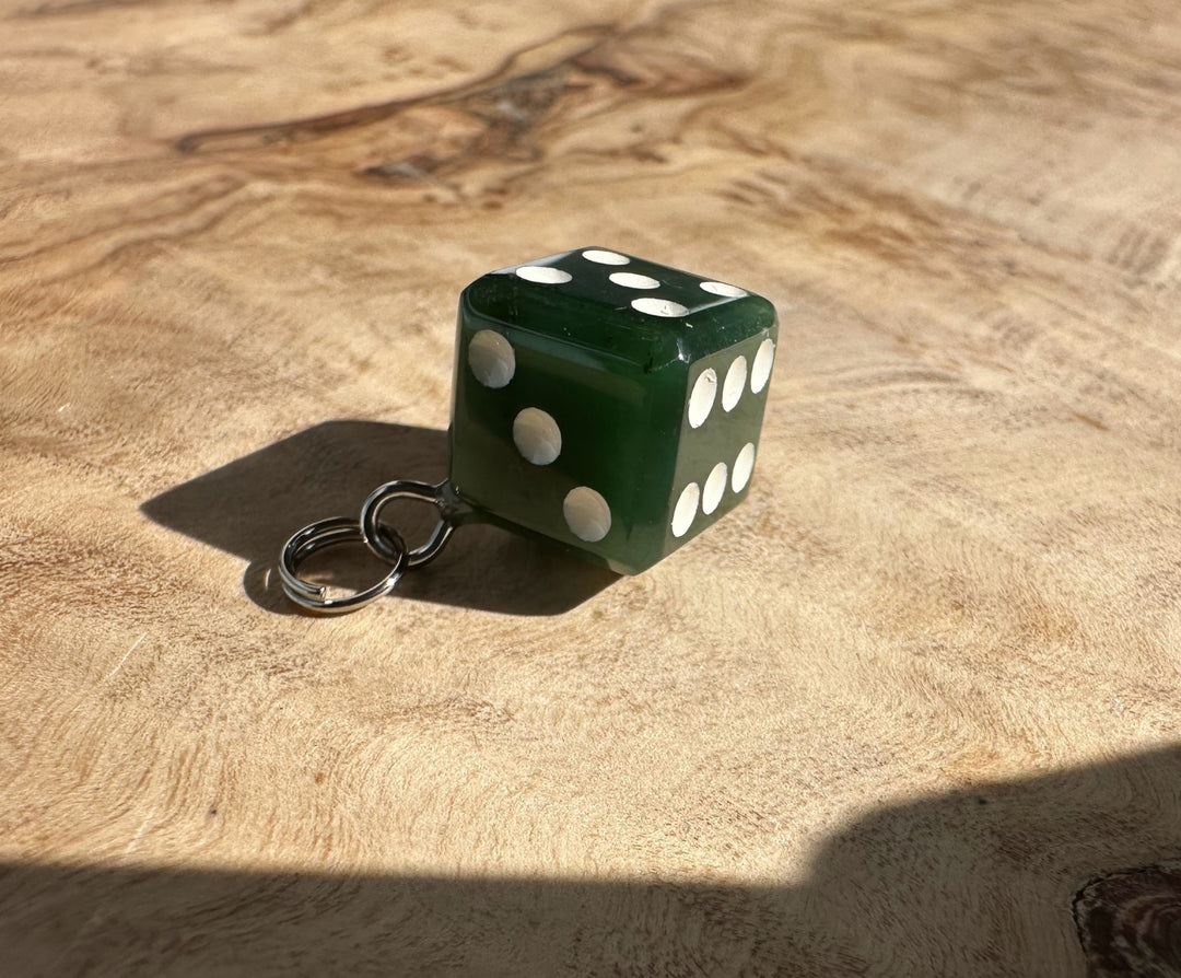 Green jade dice charm with white pips and a metal keyring on a wooden surface.
