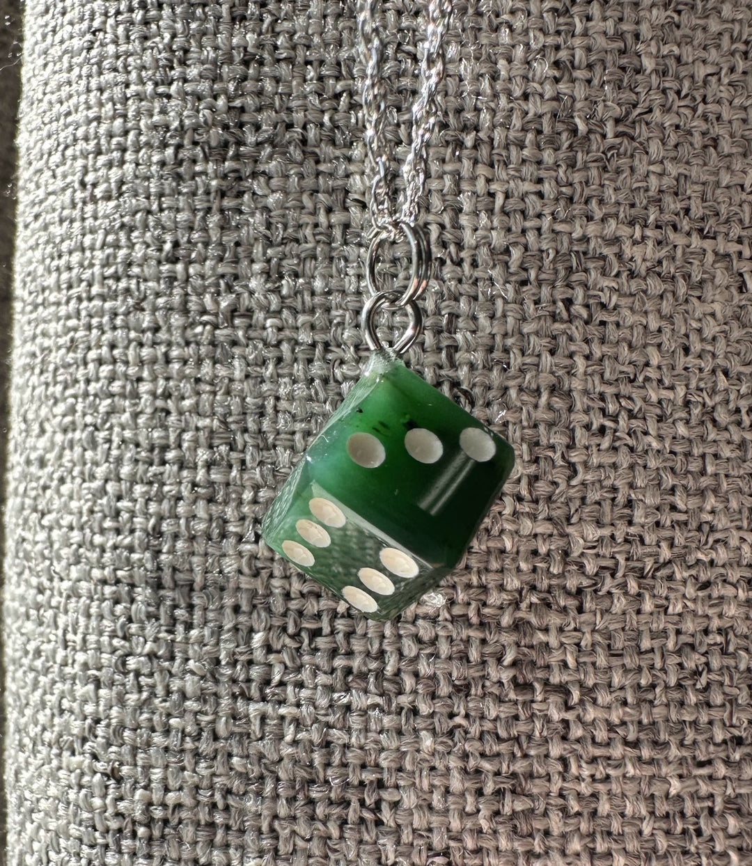 Green dice charm pendant on a silver chain against a textured gray background