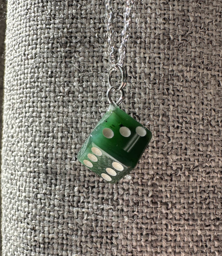 Green dice charm pendant on a silver chain against a textured gray background