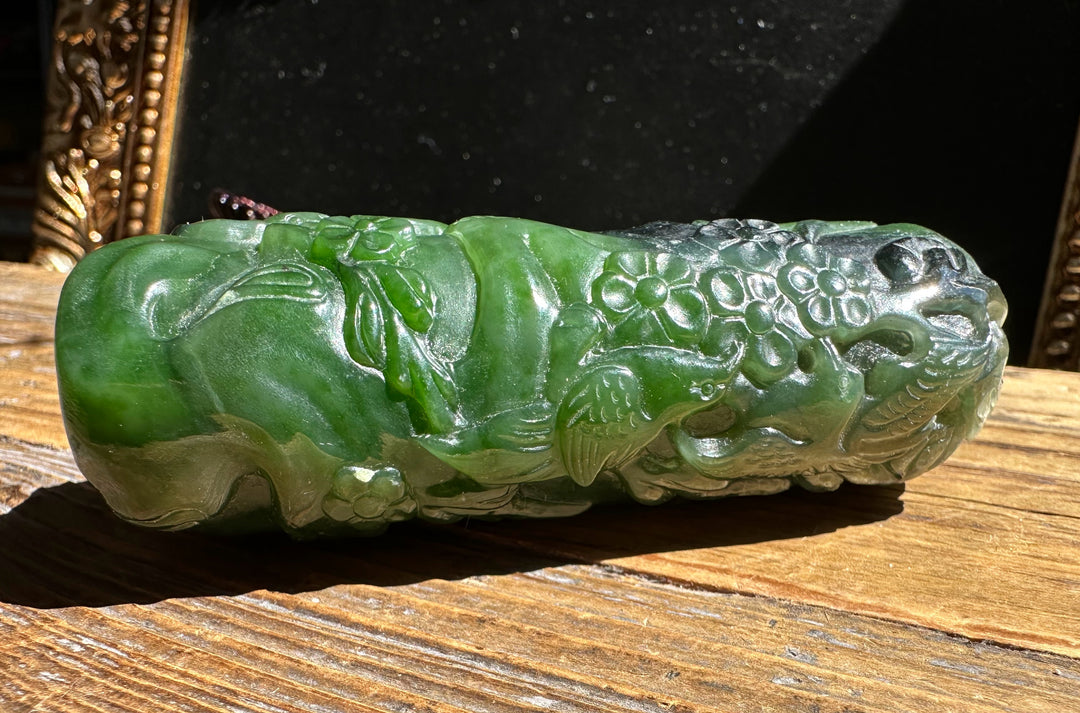 Side view of green jade handheld pendant with floral relief resting on a wood surface