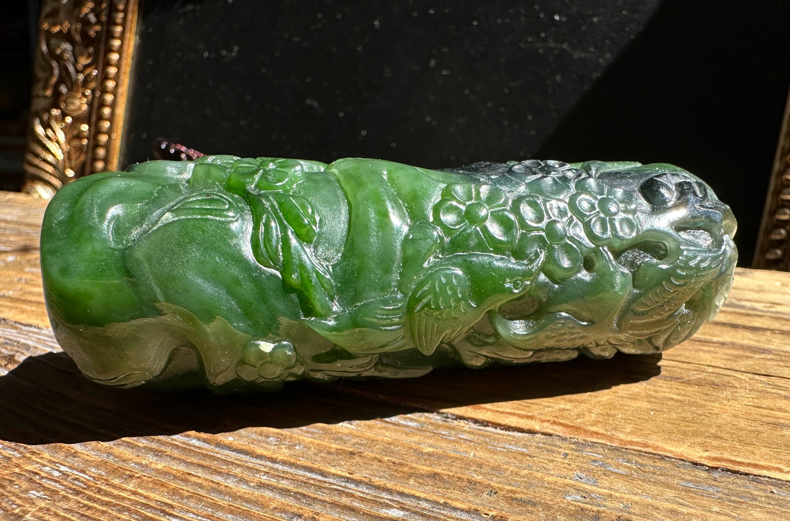 Side view of green jade handheld pendant with floral relief resting on a wood surface