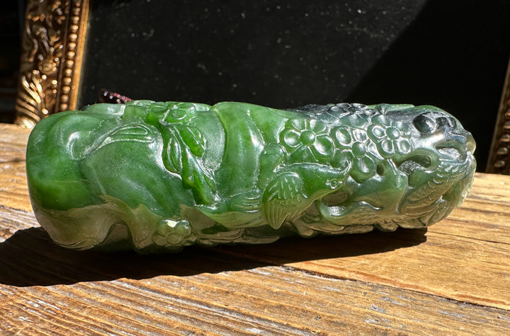Side view of green jade handheld pendant with floral relief resting on a wood surface