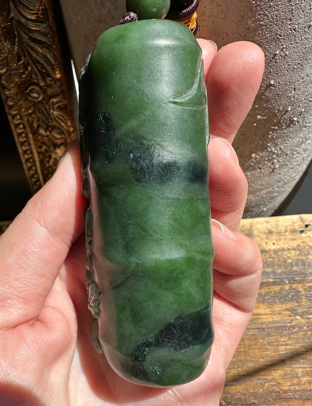 Side view of the carved green jade pendant showing detailed relief along its length.