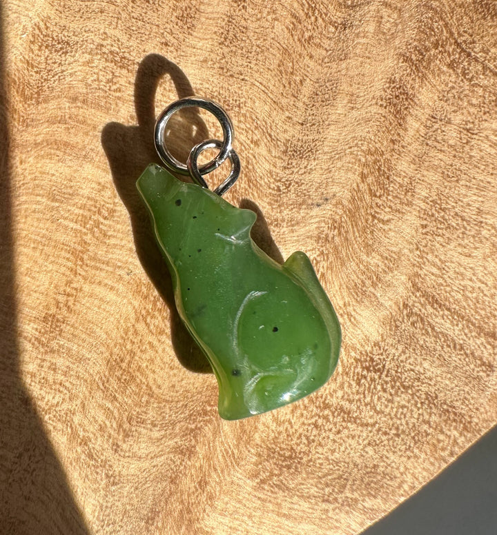 Green wolf charm pendant with a metal loop bail on a tan fabric surface