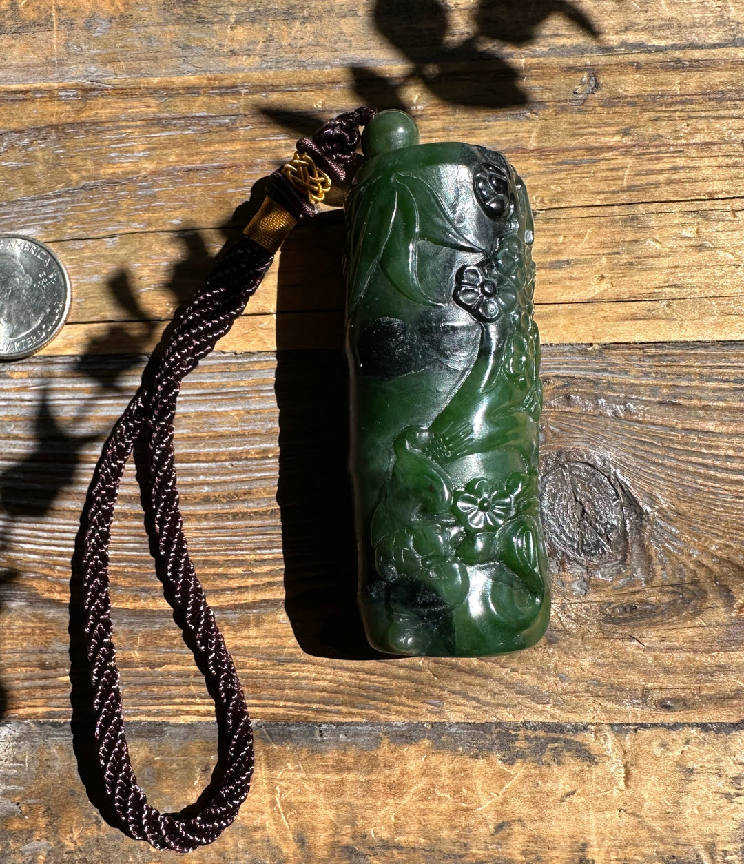 Handheld green Canadian jade pendant carved with flowers and leaves with a braided cord on wood