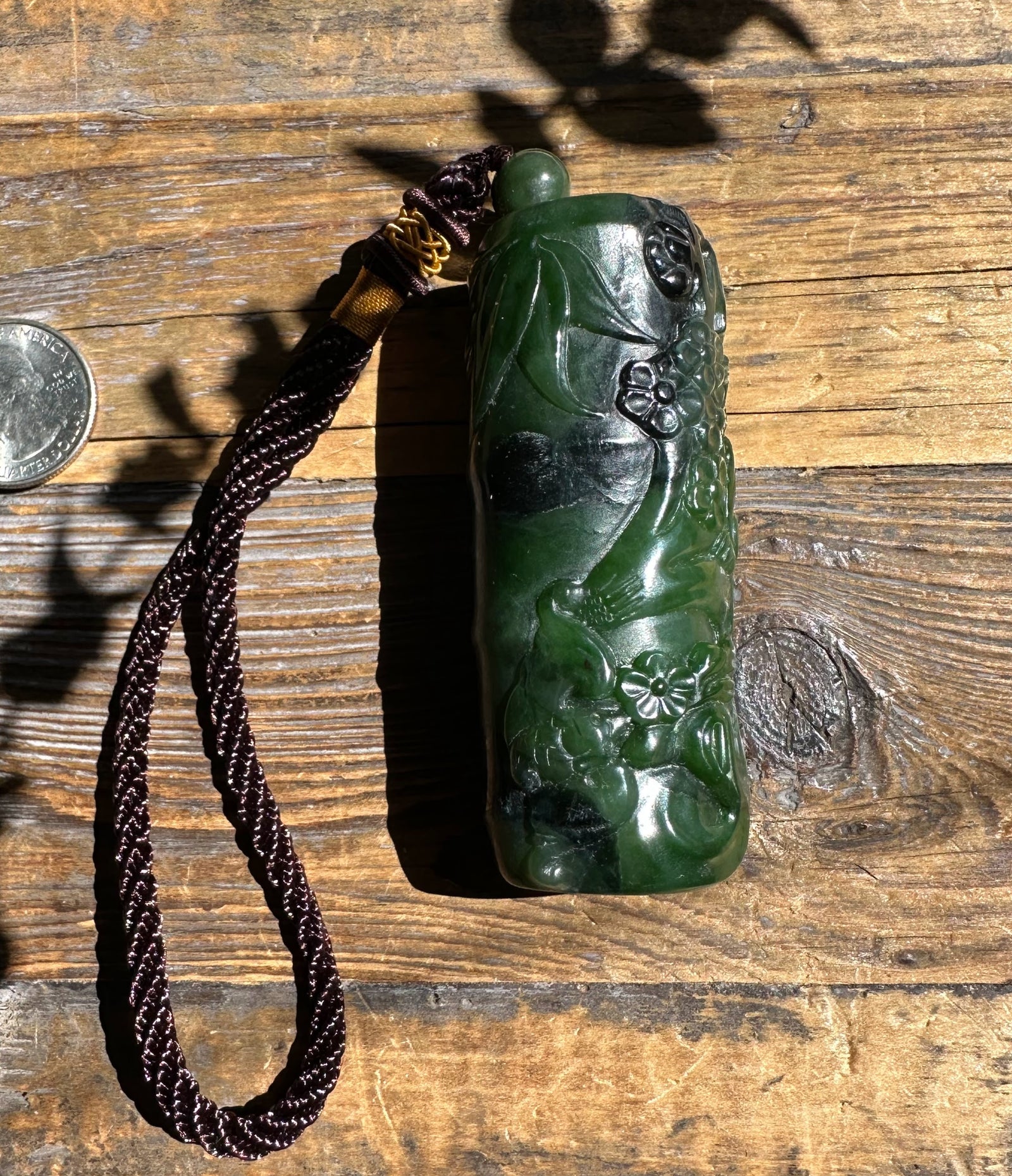 Handheld green Canadian jade pendant carved with flowers and leaves with a braided cord on wood