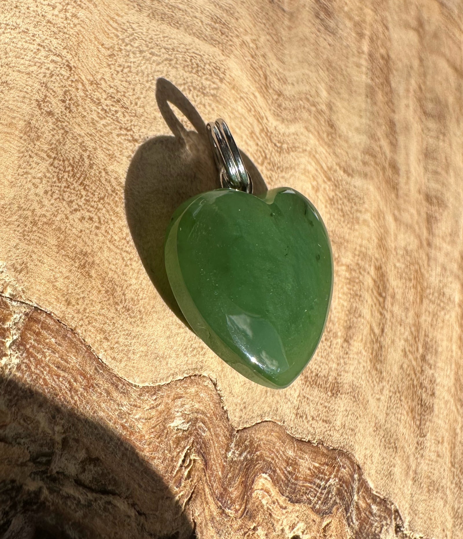 Green heart shaped pendant with a silver bail resting on textured wood