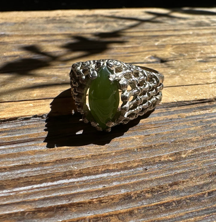 Jade ring with marquise green center stone and a textured silver cage setting on a sunlit wooden surface.