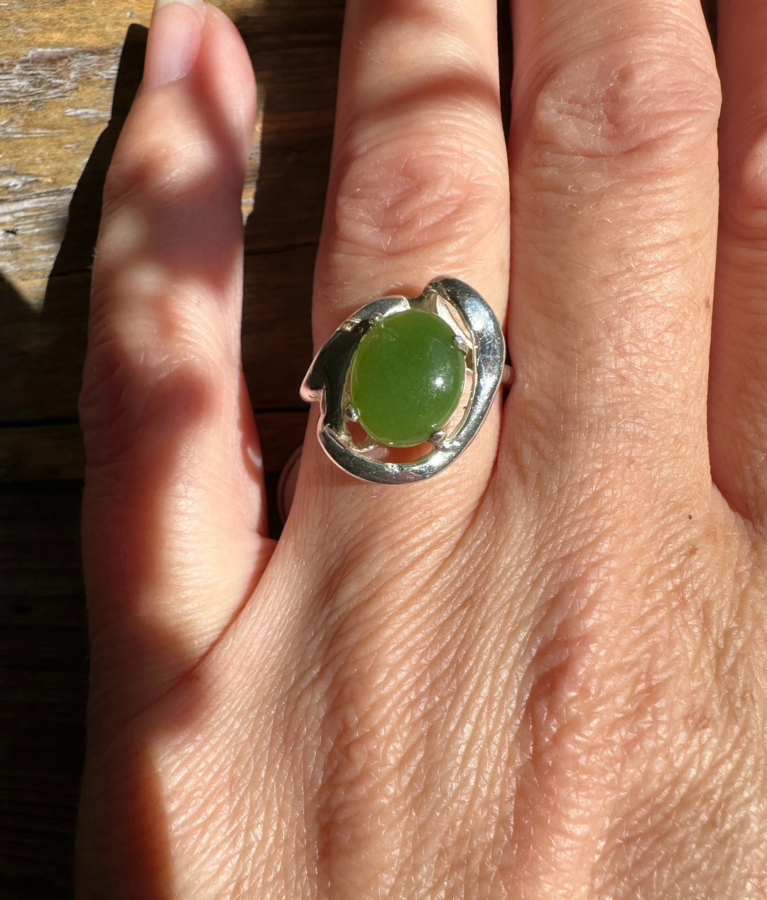 Silver Jade Ring with a green jade cabochon on a finger against a sunlit wooden surface