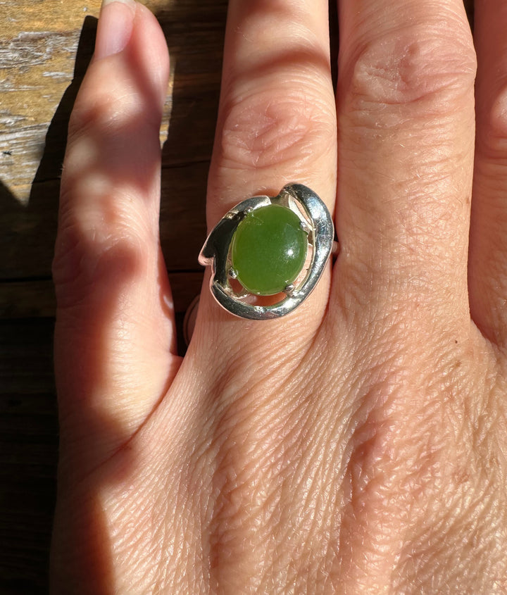 Silver Jade Ring with a green jade cabochon on a finger against a sunlit wooden surface