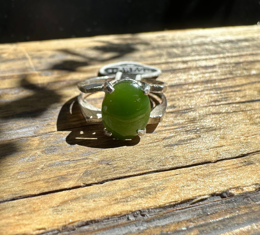 Silver ring with an oval green jade cabochon resting on a wooden surface