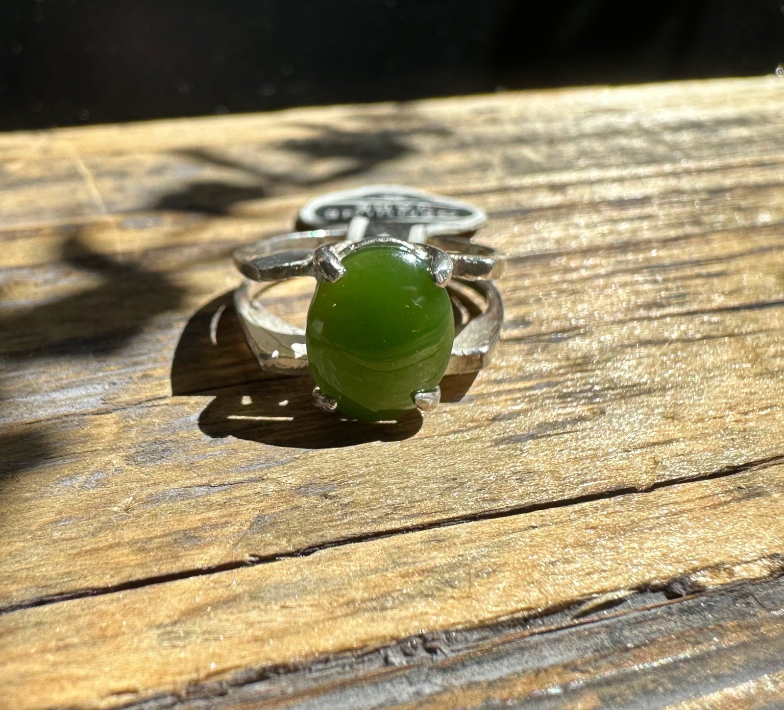 Silver ring with an oval green jade cabochon resting on a wooden surface