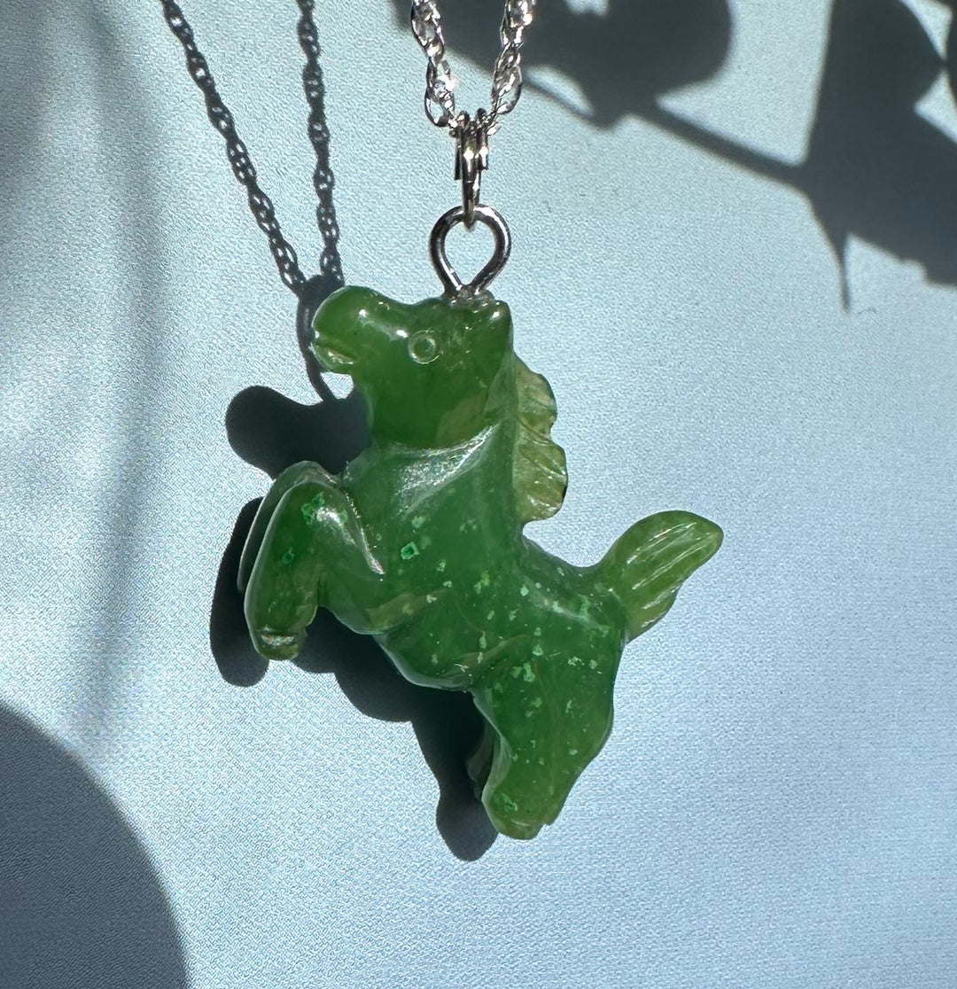 Bright green jade horse pendant on a silver chain against a blue background