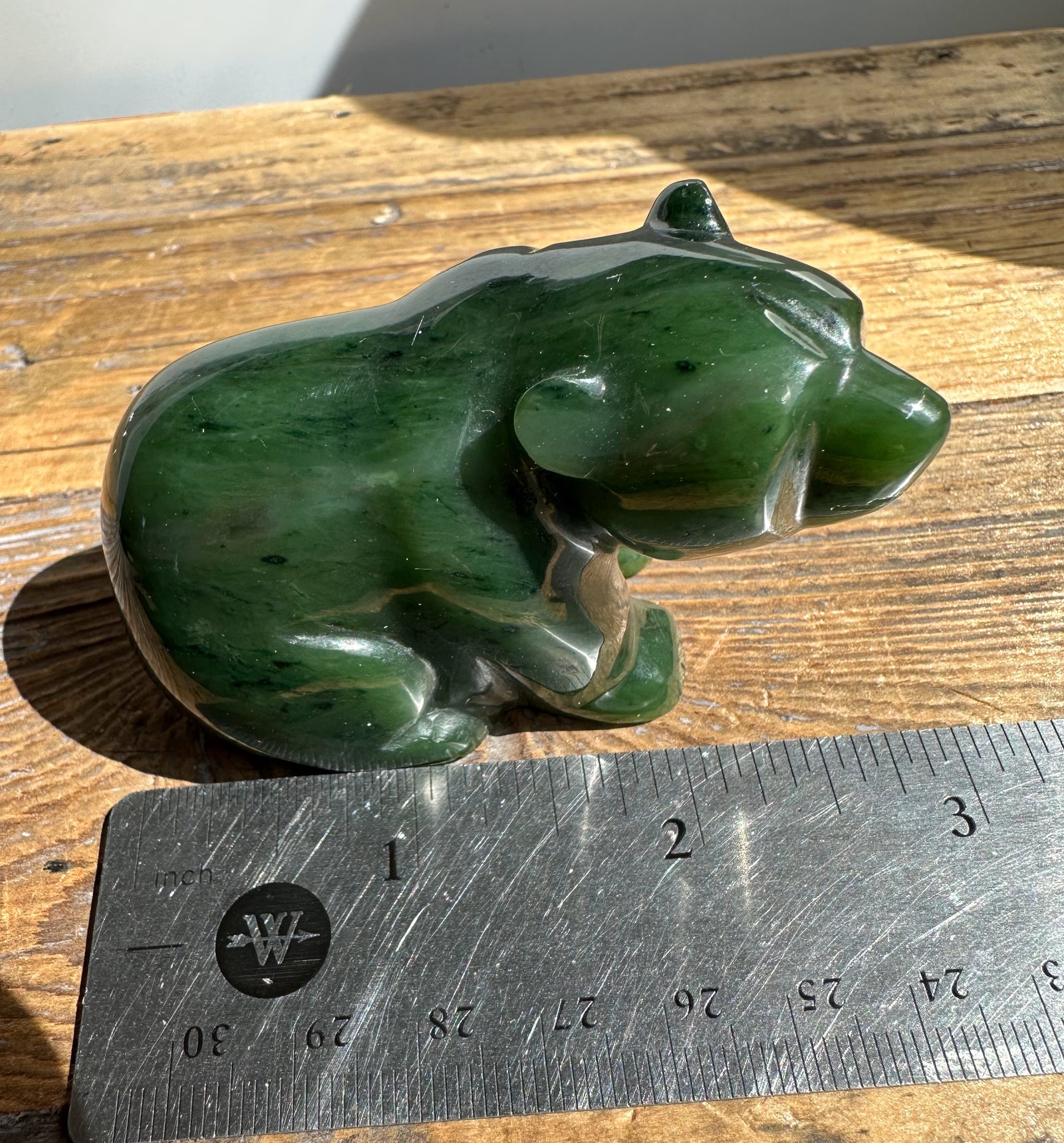 Green jade bear sculpture with a ruler for scale on a wooden surface