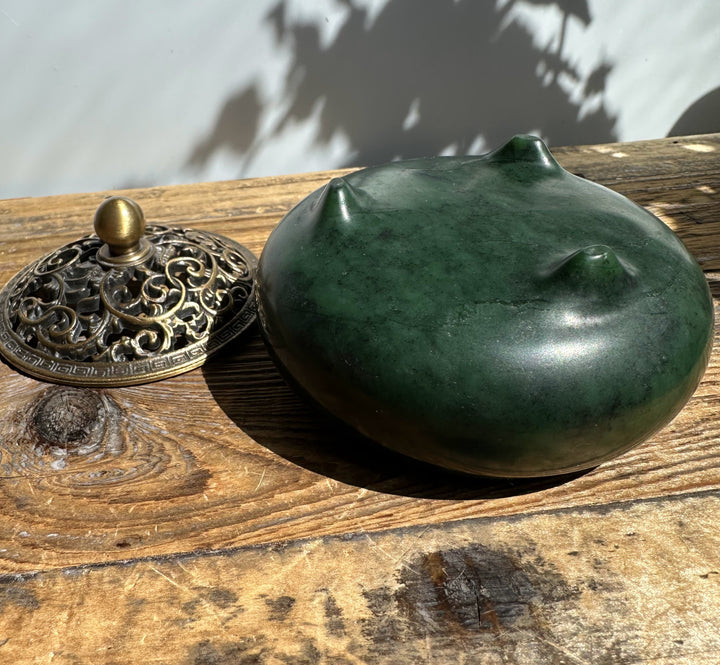 Nephrite jade incense burner with ornate brass lid removed and resting beside the green bowl on a wood surface