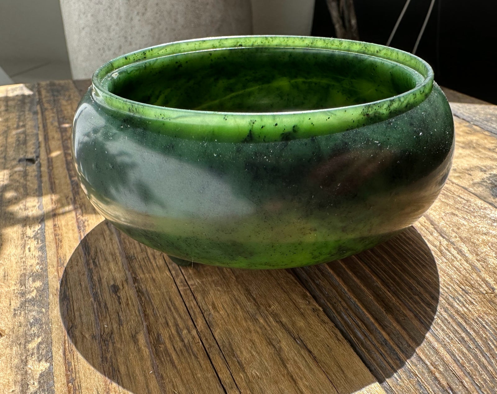 Glossy nephrite jade incense burner bowl in deep green with subtle marbling, resting on a weathered wooden surface.