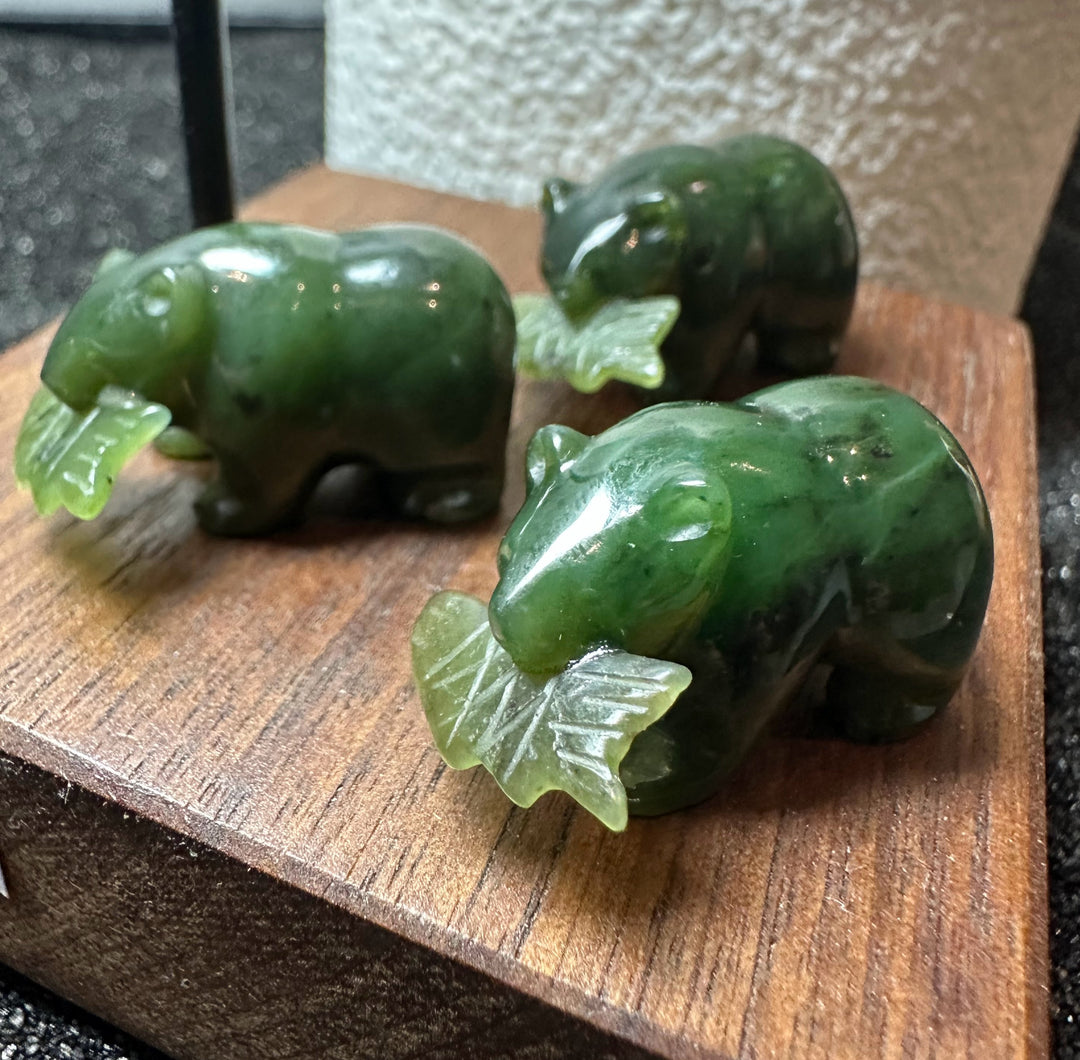 Three green jade bear figurines each holding a pale jade fish in its mouth on a wooden display block