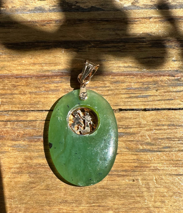 Vintage green jade good luck pendant in an oval shape with a circular metal inset at the center on a bail