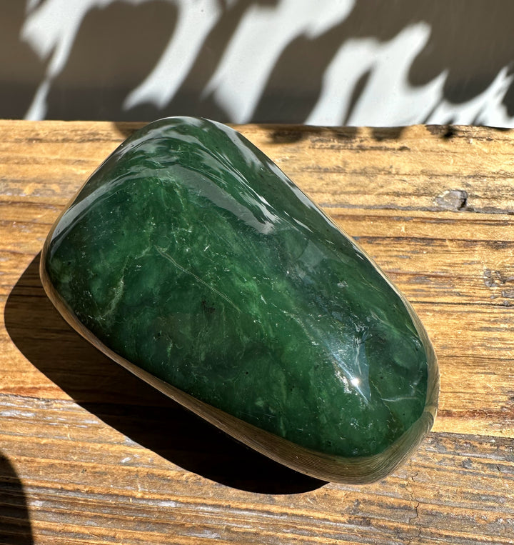Polished green jade specimen with rounded shape resting on a wooden surface