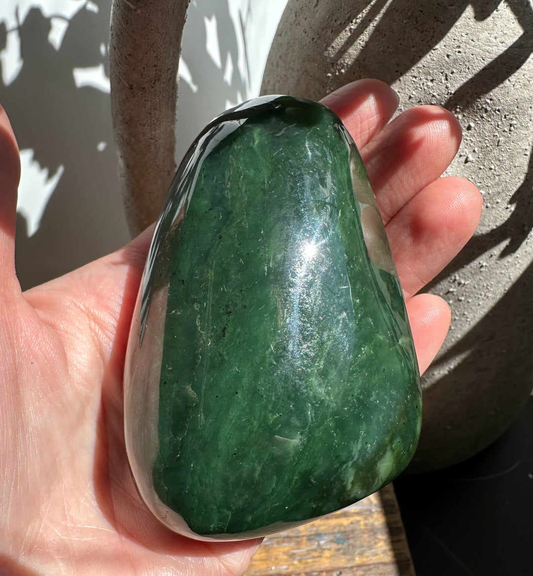 Hand holding a polished green jade stone with a glossy surface in bright outdoor light