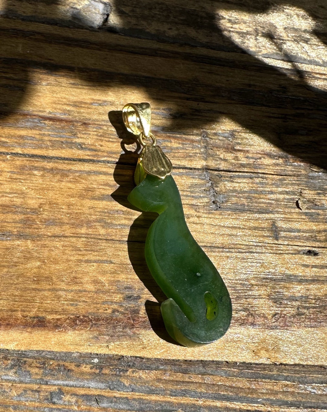 Green jade cat pendant with a gold bail resting on weathered wood