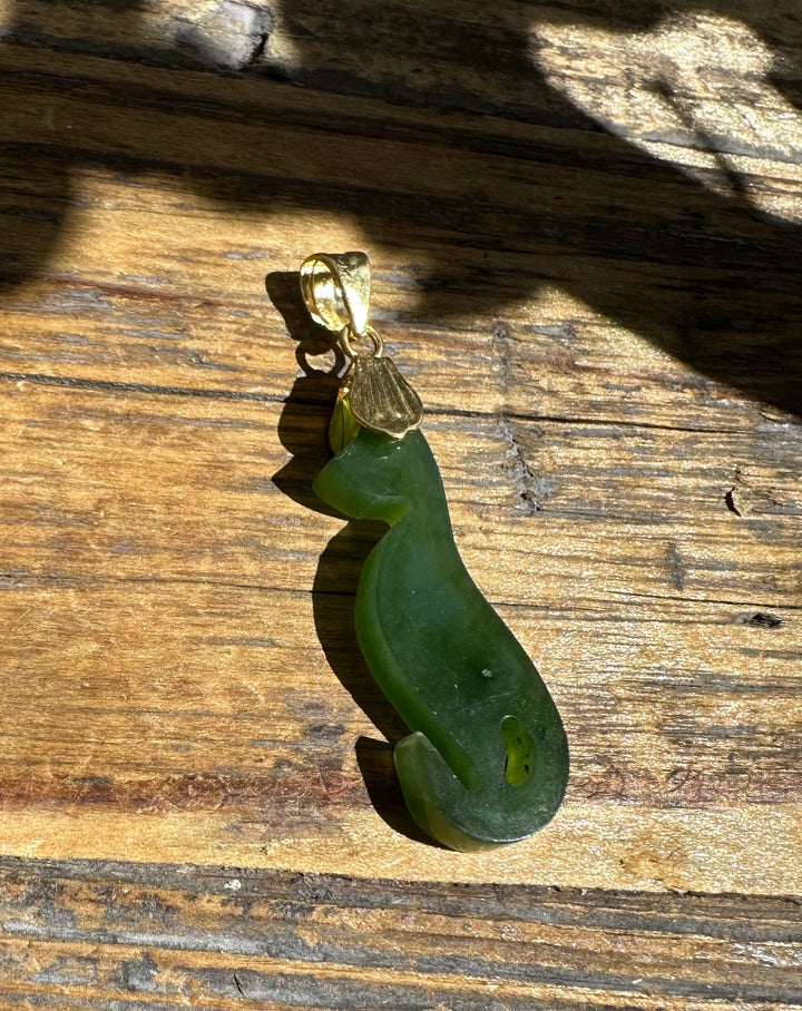 Green jade cat pendant with a gold bail resting on weathered wood