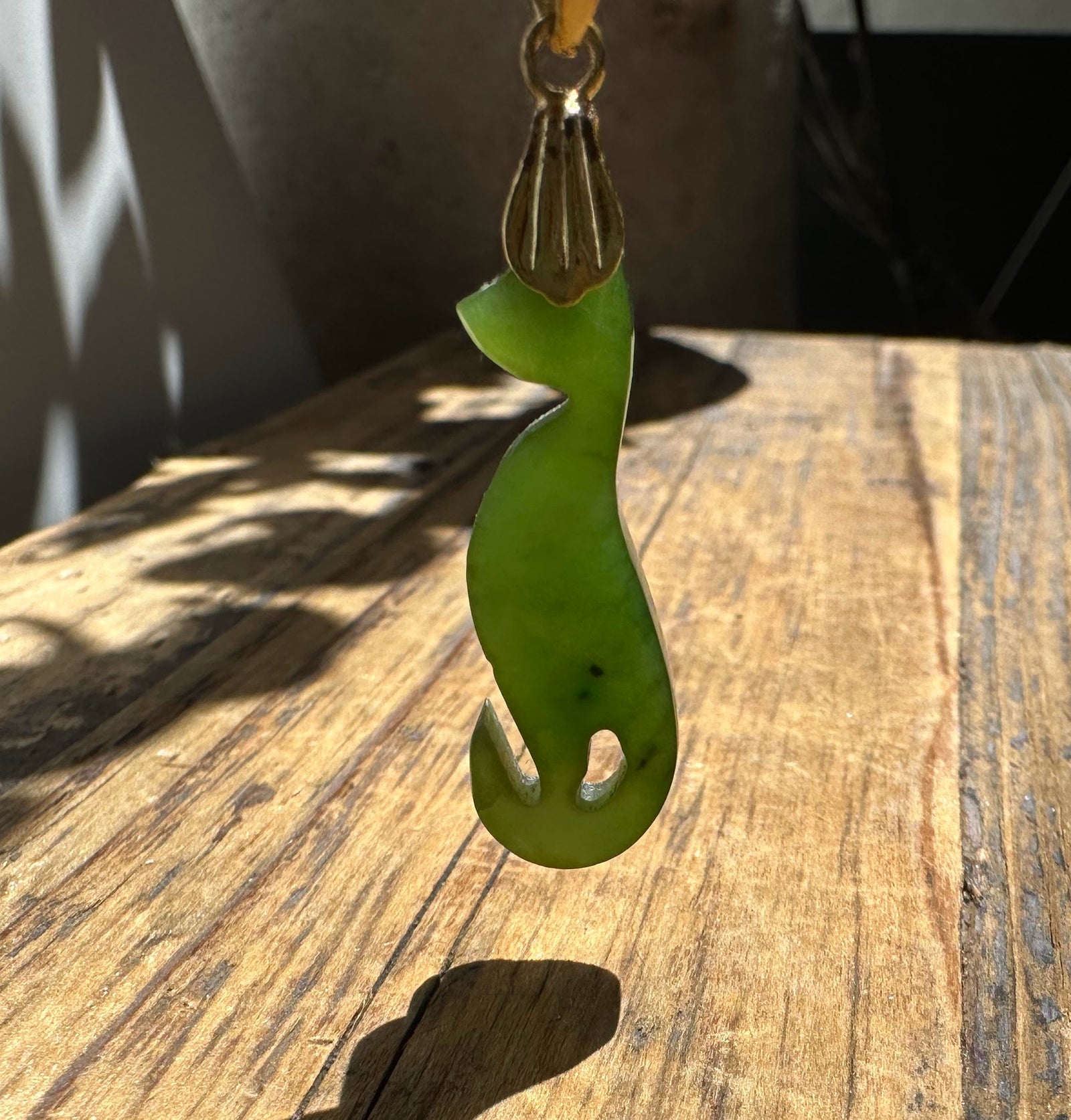 Green jade cat pendant carved in a sleek silhouette with a decorative gold bail at the top