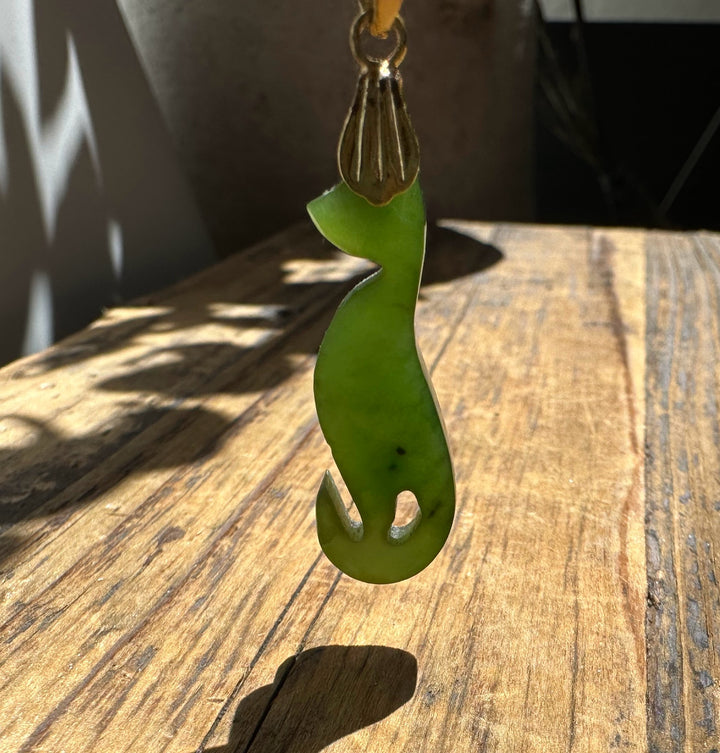 Green jade cat pendant carved in a sleek silhouette with a decorative gold bail at the top