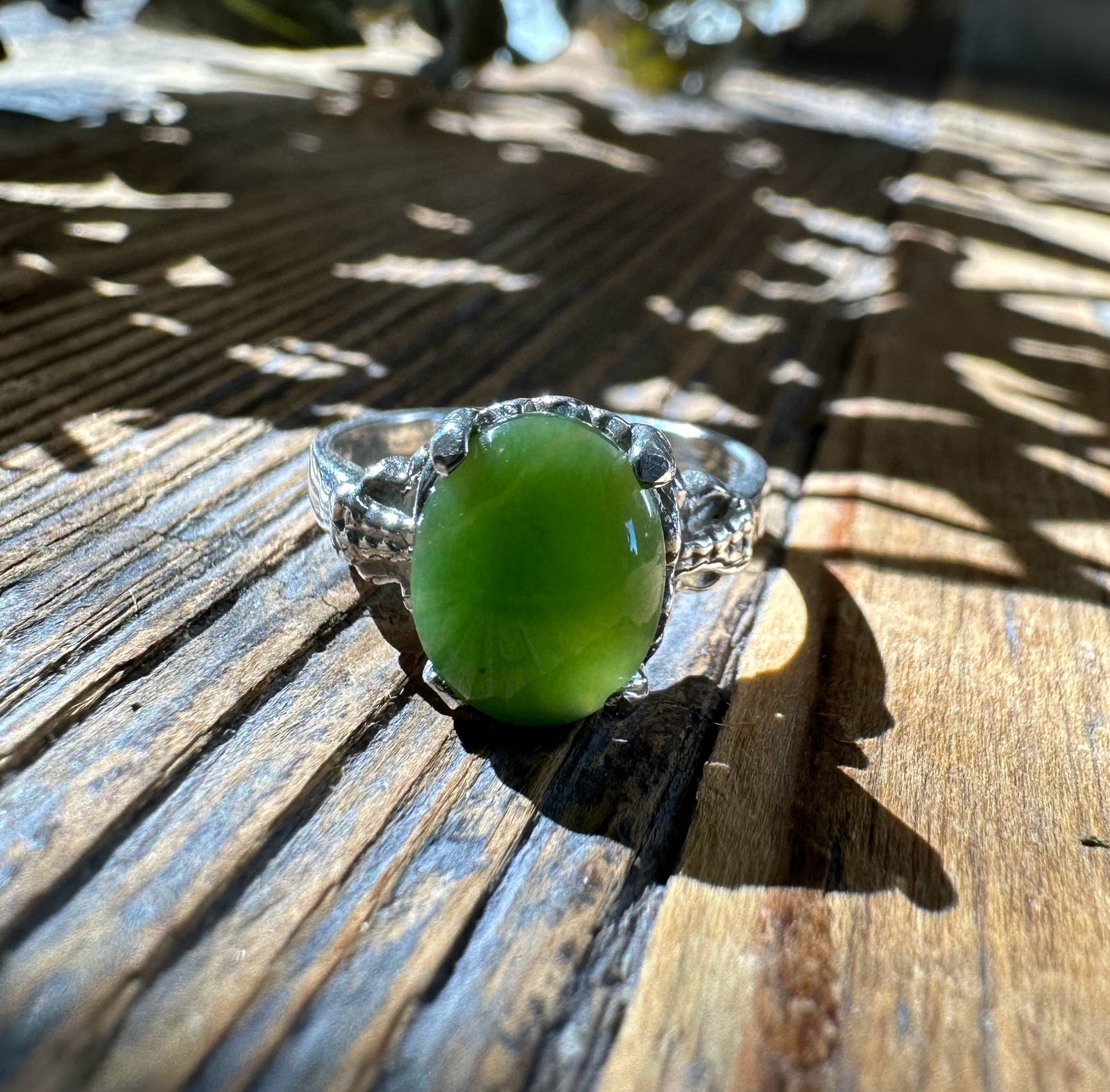 Canadian Jade Ring with an oval green jade set in a silver claw band on sunlit weathered wood