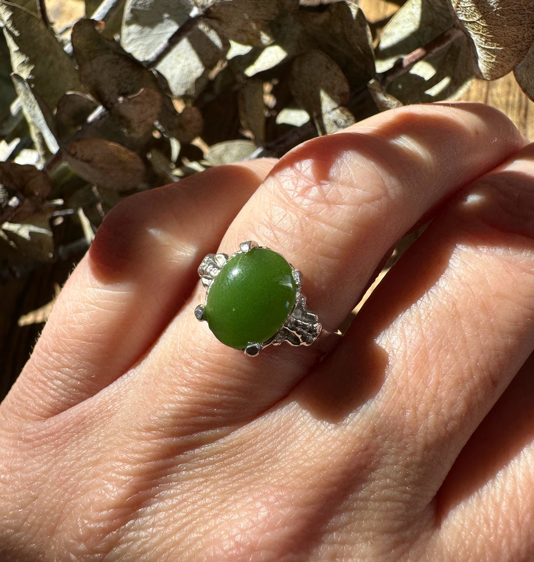 Close up of Canadian Jade Ring on finger with round green jade cabochon and silver prong setting with small accent stones.
