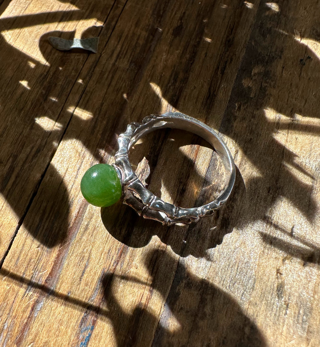 Canadian Jade Ring featuring a bright green jade sphere in a jagged silver band on a wooden surface