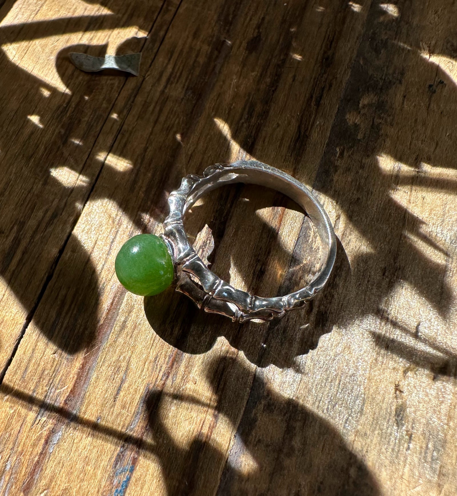 Canadian Jade Ring featuring a bright green jade sphere in a jagged silver band on a wooden surface