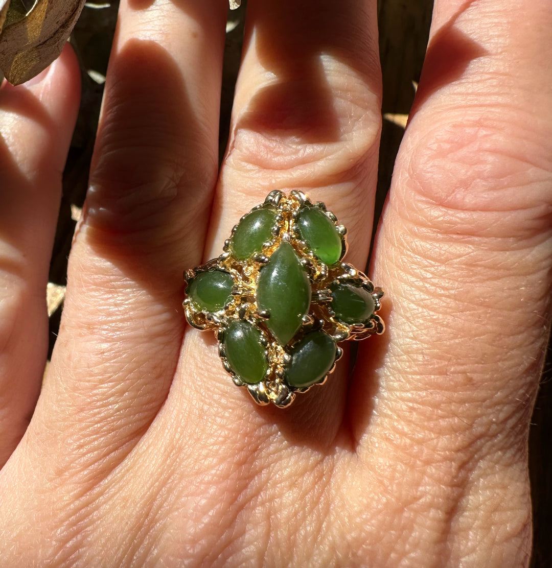 Close-up of a vintage jade ring with a marquise green centerpiece surrounded by smaller jade stones in a gold setting