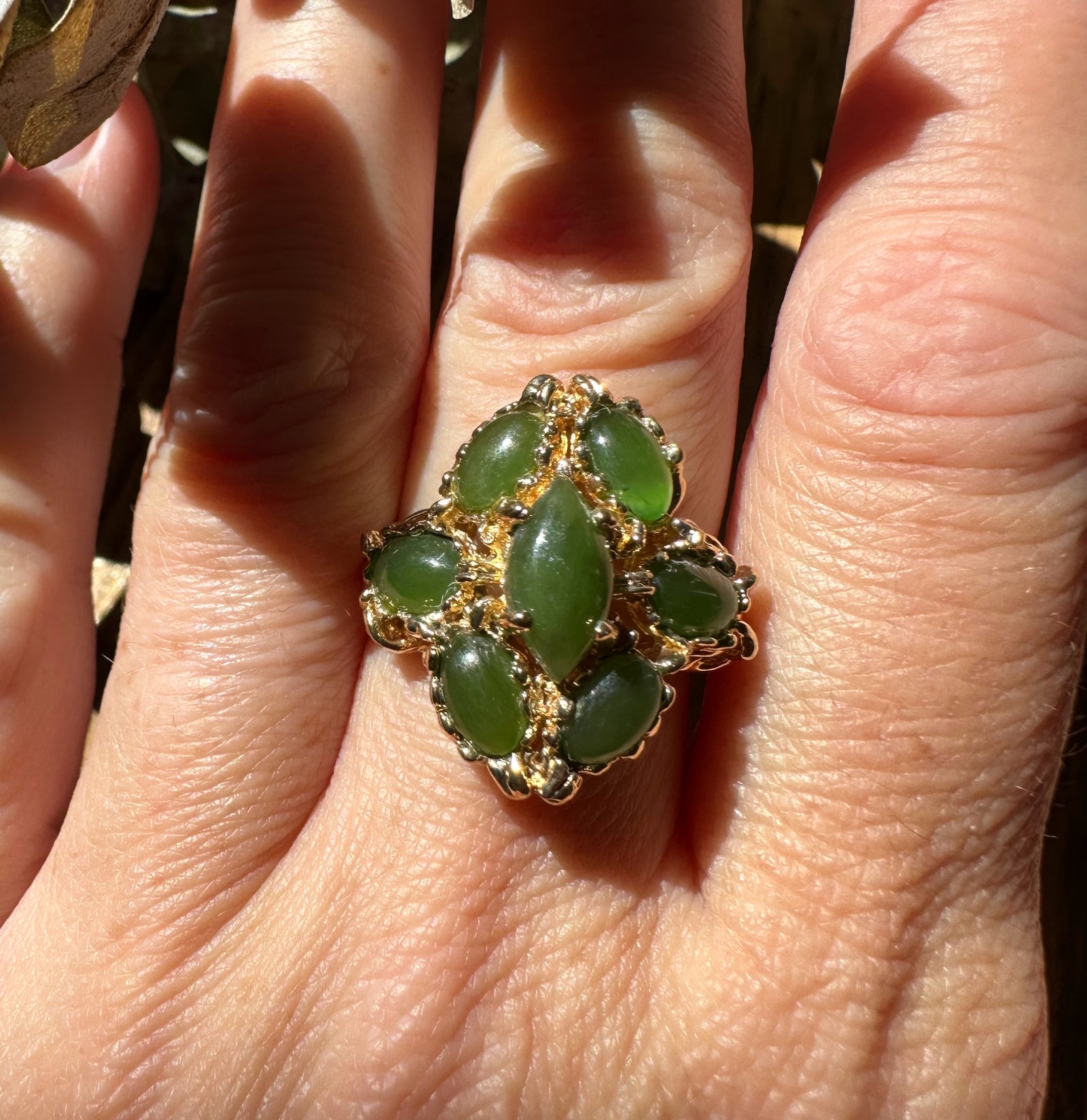 Close-up of a vintage jade ring with a marquise green centerpiece surrounded by smaller jade stones in a gold setting