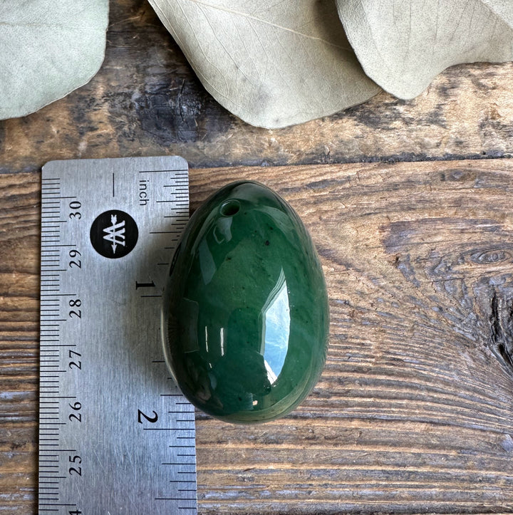 Canadian nephrite yoni egg shown beside a ruler for scale on a wooden surface, smooth green stone