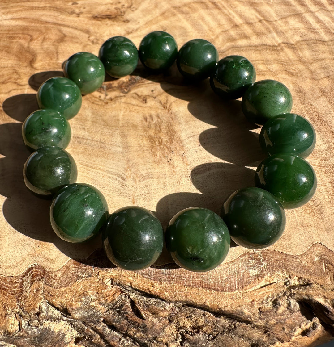 Green nephrite jade bead bracelet with 14mm round beads laid on a wooden surface.